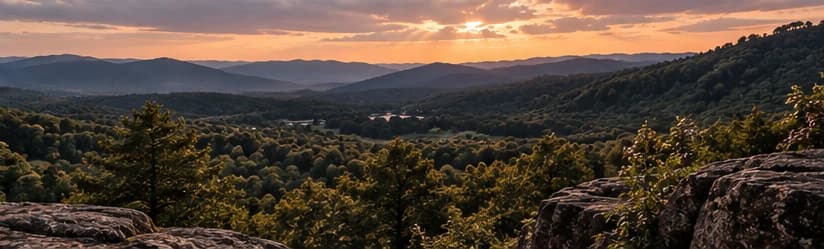 An expansive wooded mountain landscape beneath a warm evening sky